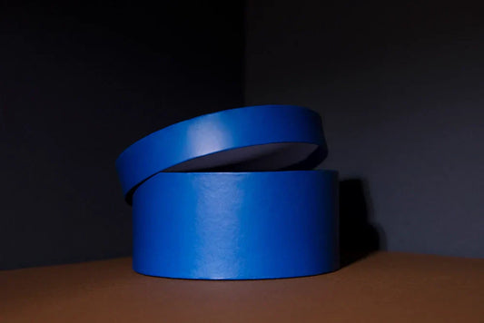 A blue cylindrical paper tube packaging box with its lid slightly open, placed against a dark background.