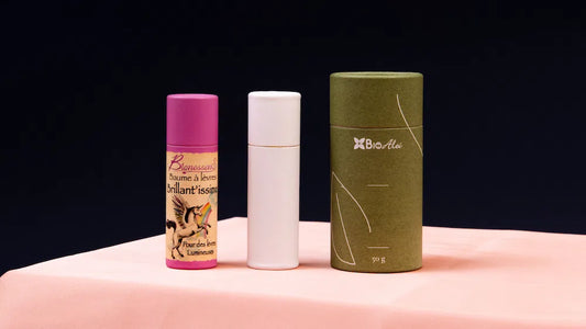 Three cylindrical paper tube packages in different colors and designs, displayed on a pink surface against a dark background.