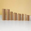 A descending lineup of cylindrical kraft paper tubes arranged from tallest to shortest on a surface, with a contrasting yellow backdrop highlighting their uniform brown tones.