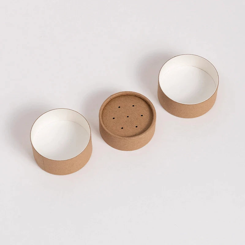 An image of a singular paper shaker tube, displayed in three separate parts, showcasing the top, perforated lid, main body, and the interior against a white background.