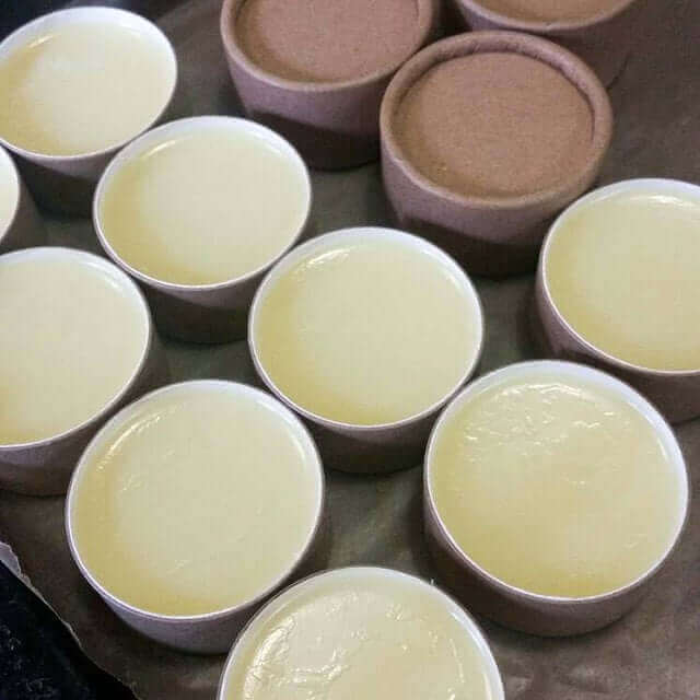 A collection of open brown kraft paper tubes filled with smooth yellow lip balm, displayed together, showcasing handmade personal care products on a dark countertop.