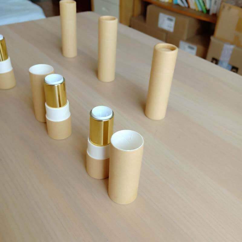 Several pale beige paper tubes are standing vertically on a wooden surface, with two horizontally placed in the foreground showing a metallic gold-colored interior.
