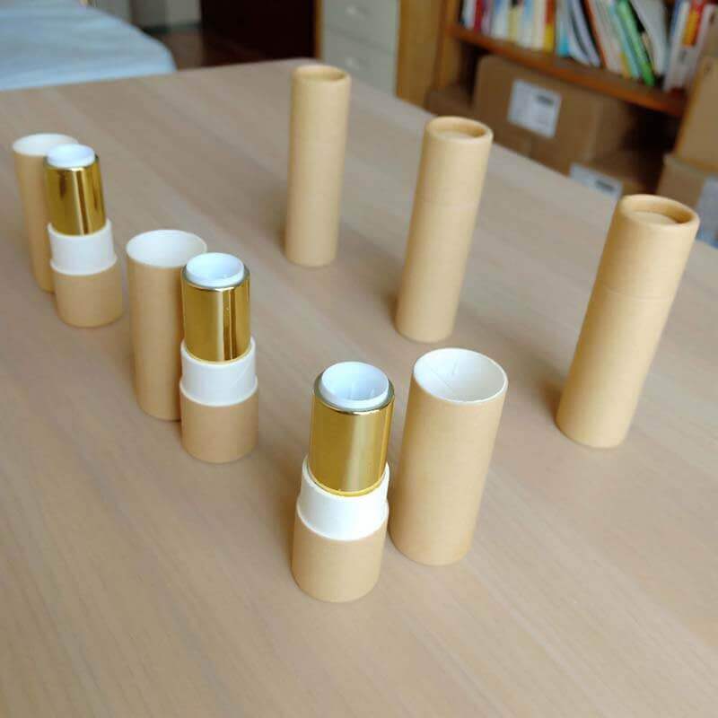 Several pale beige paper tubes are standing vertically on a wooden surface, with two horizontally placed in the foreground showing a metallic gold-colored interior.